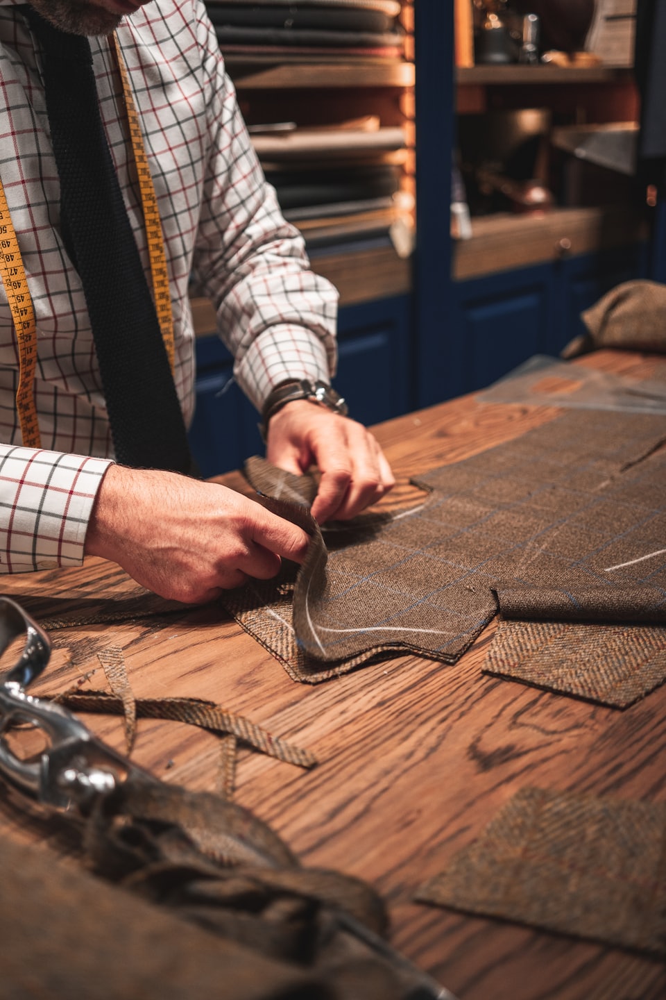 Mani di sarto lavorano tessuto di tweed su un banco da lavoro.